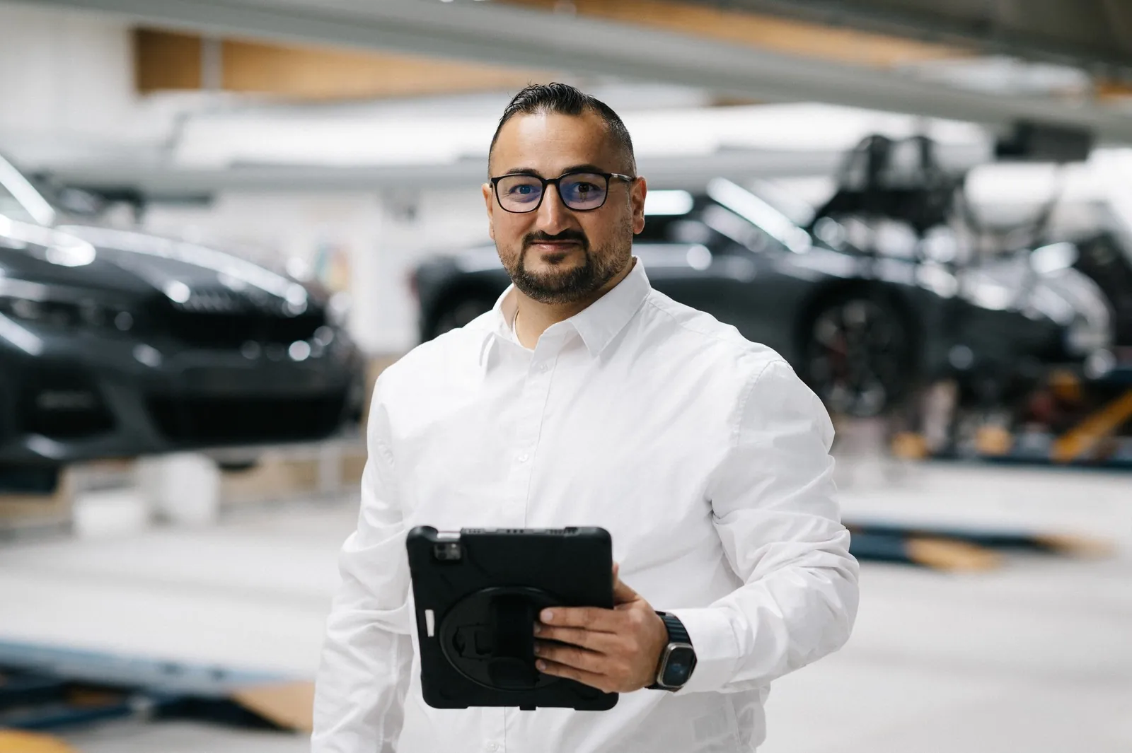 Kfz-Sachverständiger Cüneyt Kadak im weißen Hemd mit Tablet in einer Werkstatt
